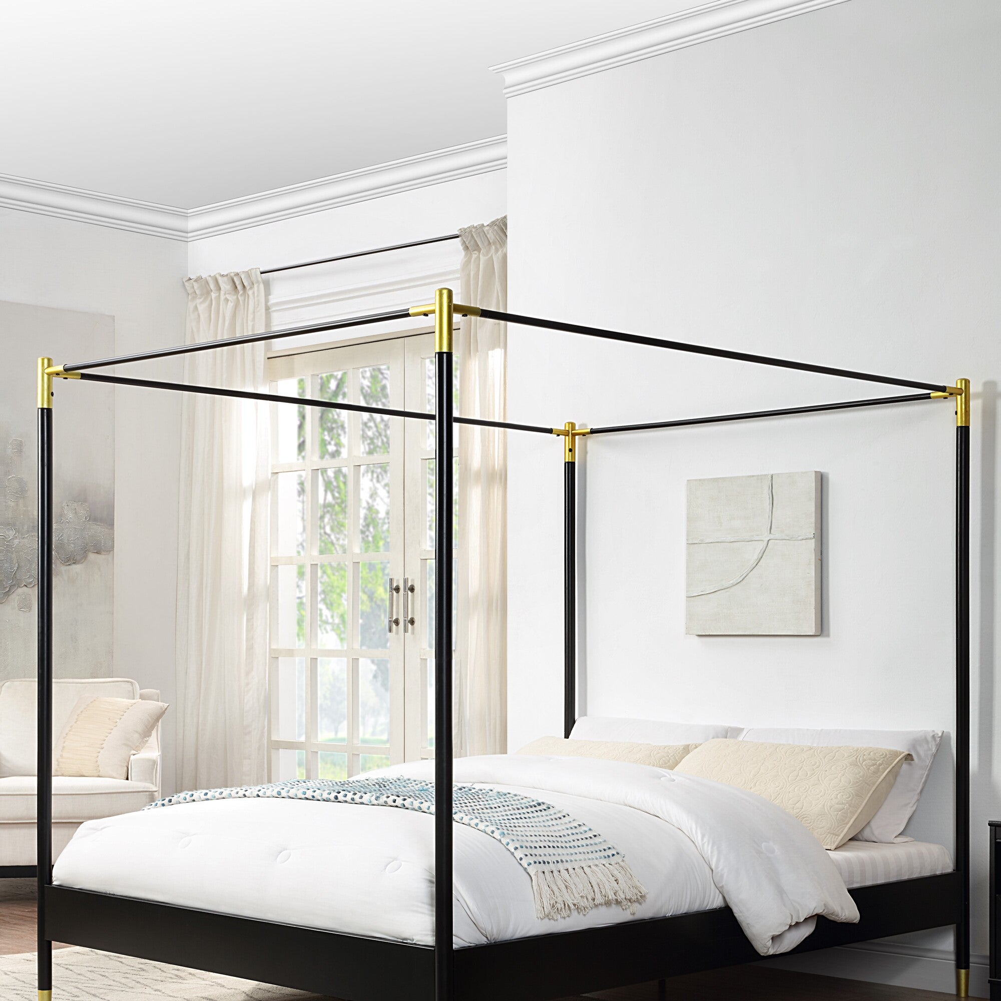 A black metal four-poster bed with gold accents at the corners, positioned in a bright room with white walls, large windows, and light curtains.