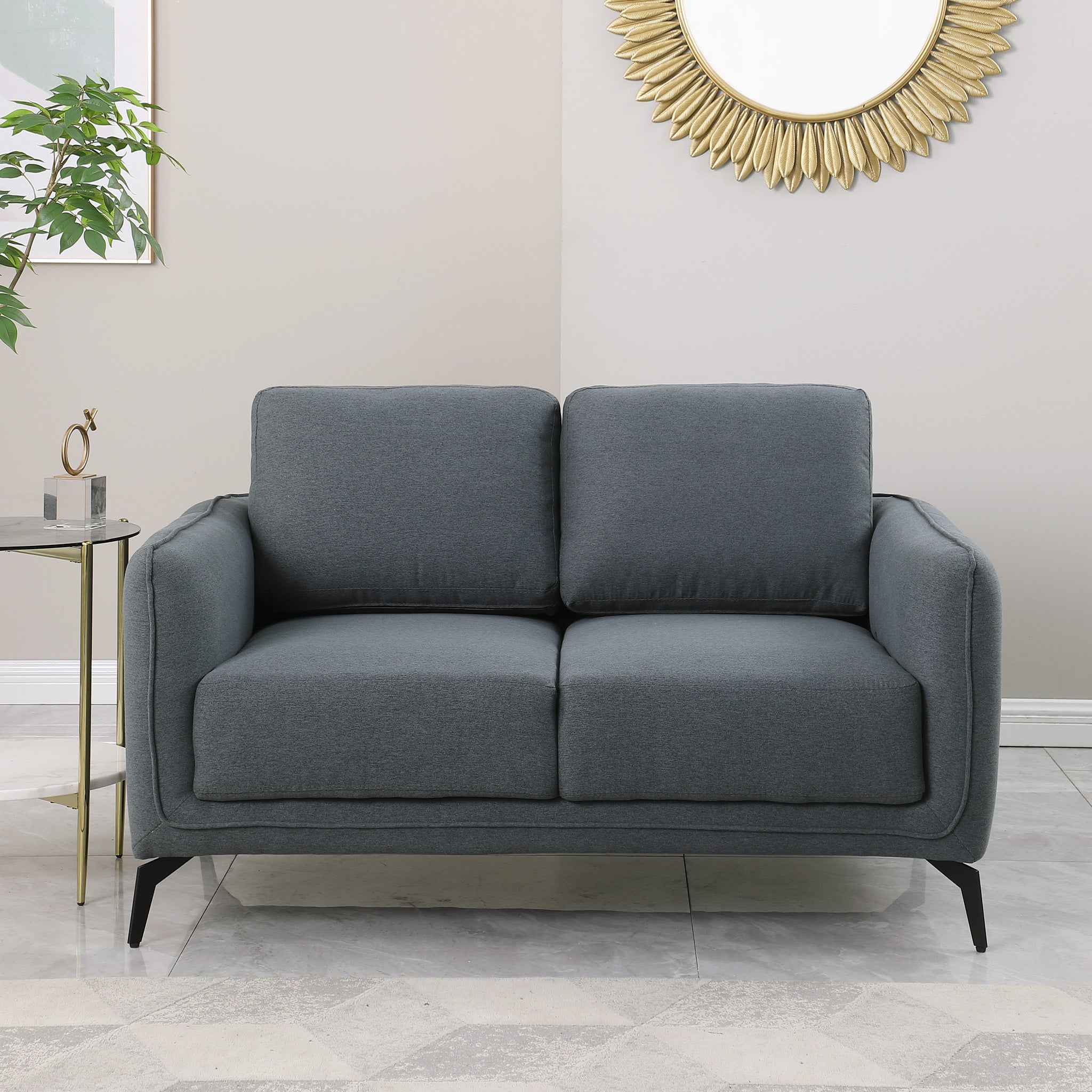 Dark grey upholstered sofa with black metal legs in a living room, featuring a round sunburst mirror and a side table with flowers.