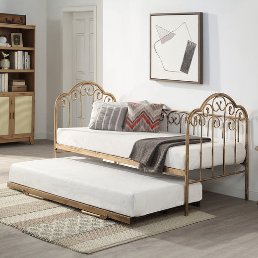 A brass metal day bed with an extended trundle is adorned with white bedding, decorative pillows, and a grey throw blanket. A geometric painting hangs above the bed.