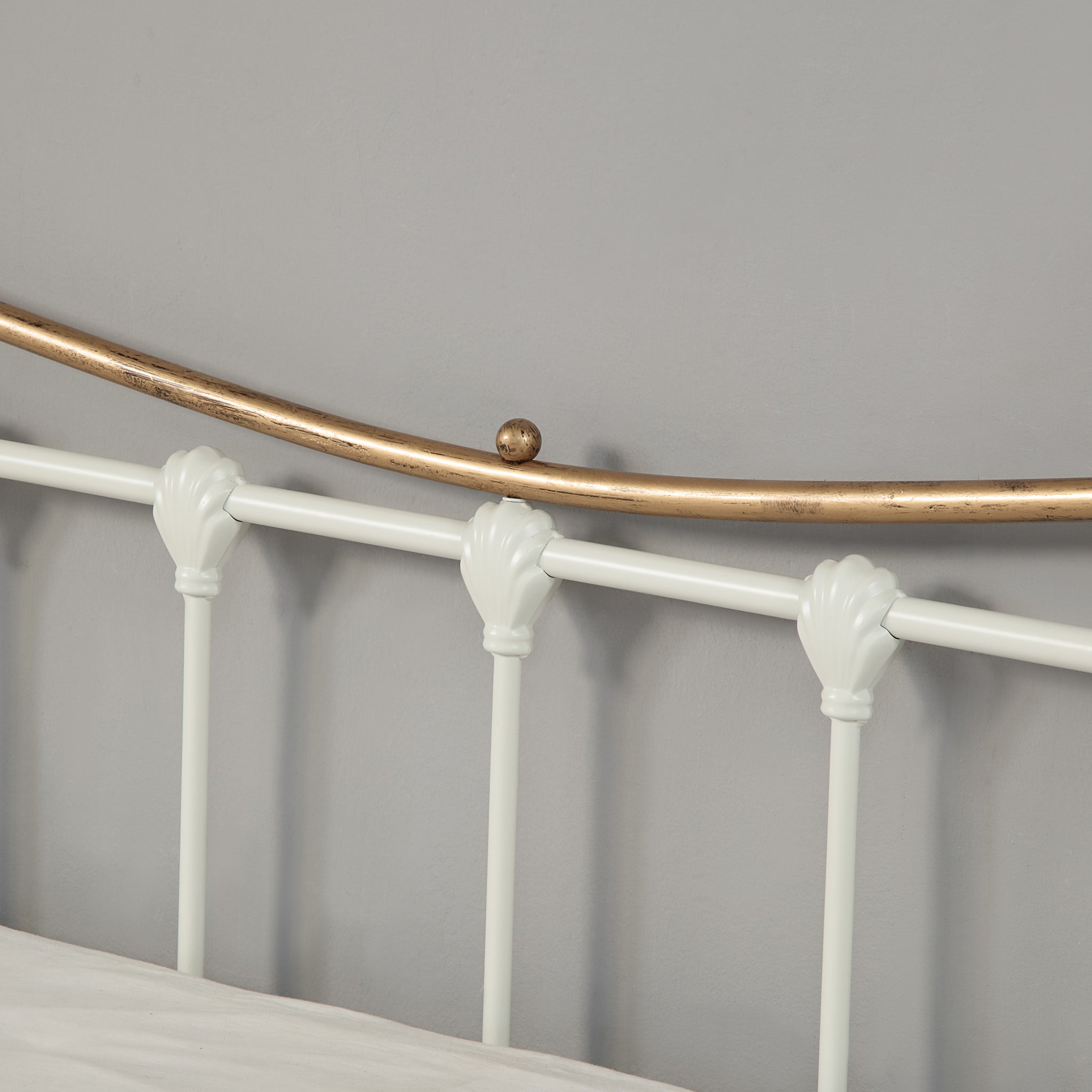 Close up view of a white and brass metal headboard.