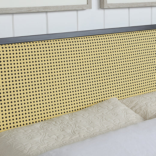 Close-up of a bed with a woven rattan headboard. The bed is made with quilted beige bedding, and the background features white paneled walls with framed artwork.