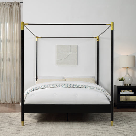 A black metal four-poster bed with gold accents on the corners and feet, set against a white wall, beside a large window with light curtains.