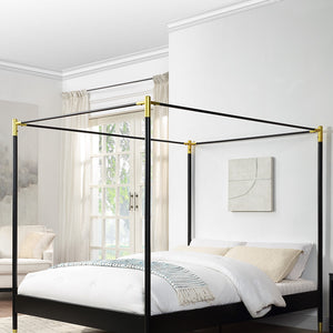 A black metal four-poster bed with gold accents at the corners, positioned in a bright room with white walls, large windows, and light curtains.