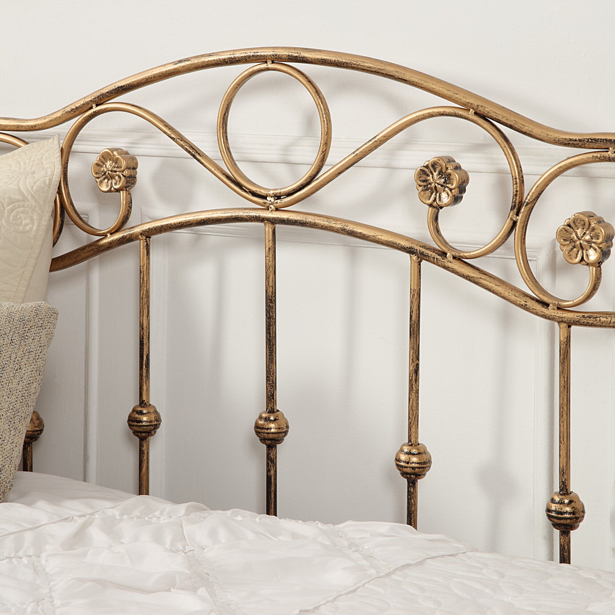 Close-up of the bronze-coloured metal daybed, showcasing intricate swirl patterns and floral accents on the headboard, against a white background.