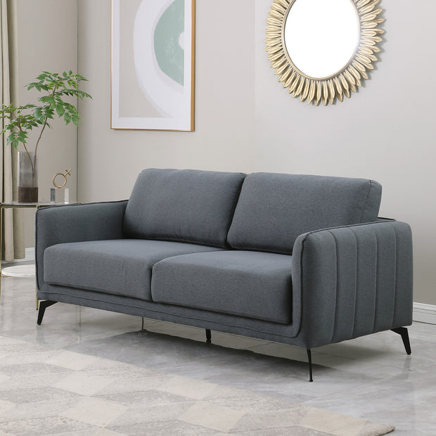 Dark grey fabric sofa with black metal legs in a grey living room, featuring a round sunburst mirror and a side table with flowers.