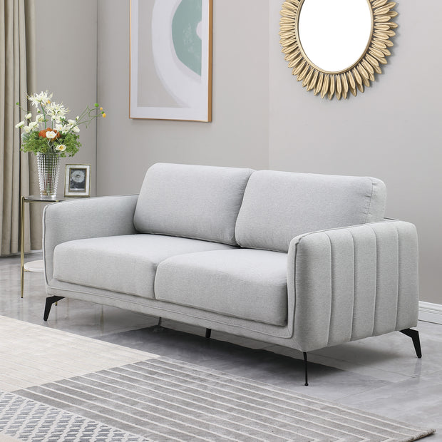 Light grey upholstered sofa with black metal legs in a grey living room, featuring a round sunburst mirror and a side table with flowers.