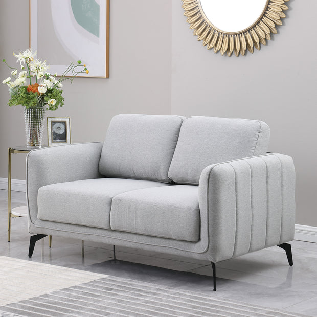 Light grey upholstered sofa with black metal legs in a grey living room, featuring a round sunburst mirror and a side table with flowers.