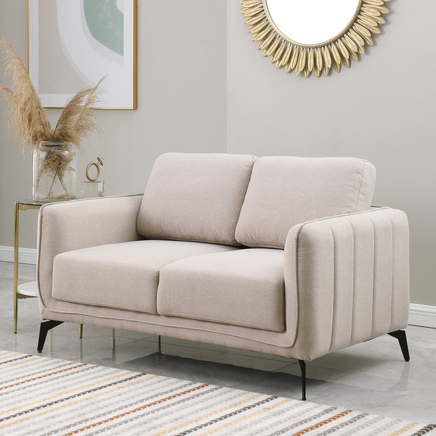 Beige fabric sofa with black metal legs in a grey living room, featuring a round sunburst mirror and a side table with flowers.