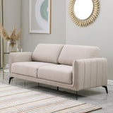 Beige fabric sofa with black metal legs in a grey living room, featuring a round sunburst mirror and a side table with flowers.