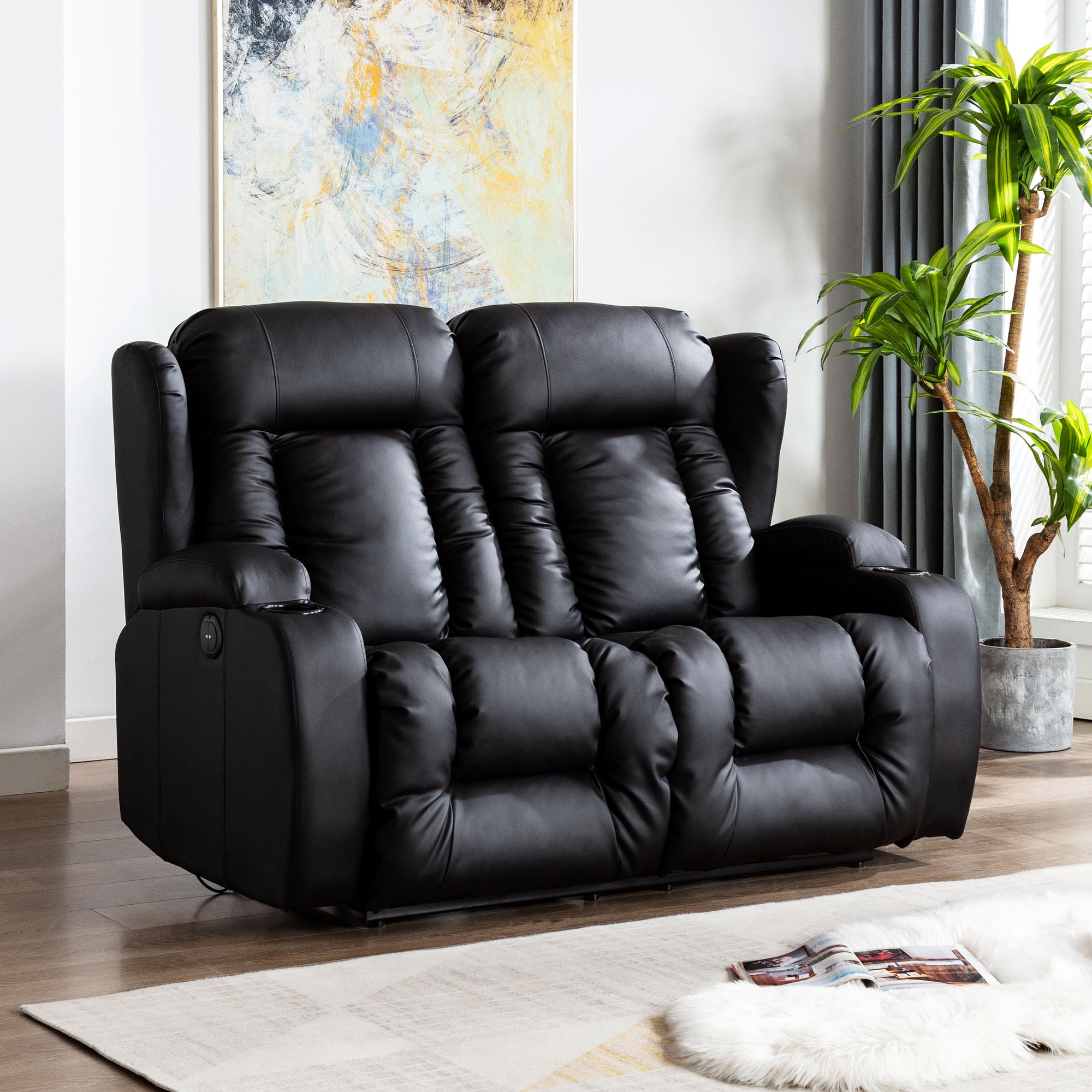 Black leather two-seater electric recliner sofa with both seats in an upright position, featuring cushioned backrests, cupholders, and side pockets, set in a living room with wooden flooring and abstract wall art.
