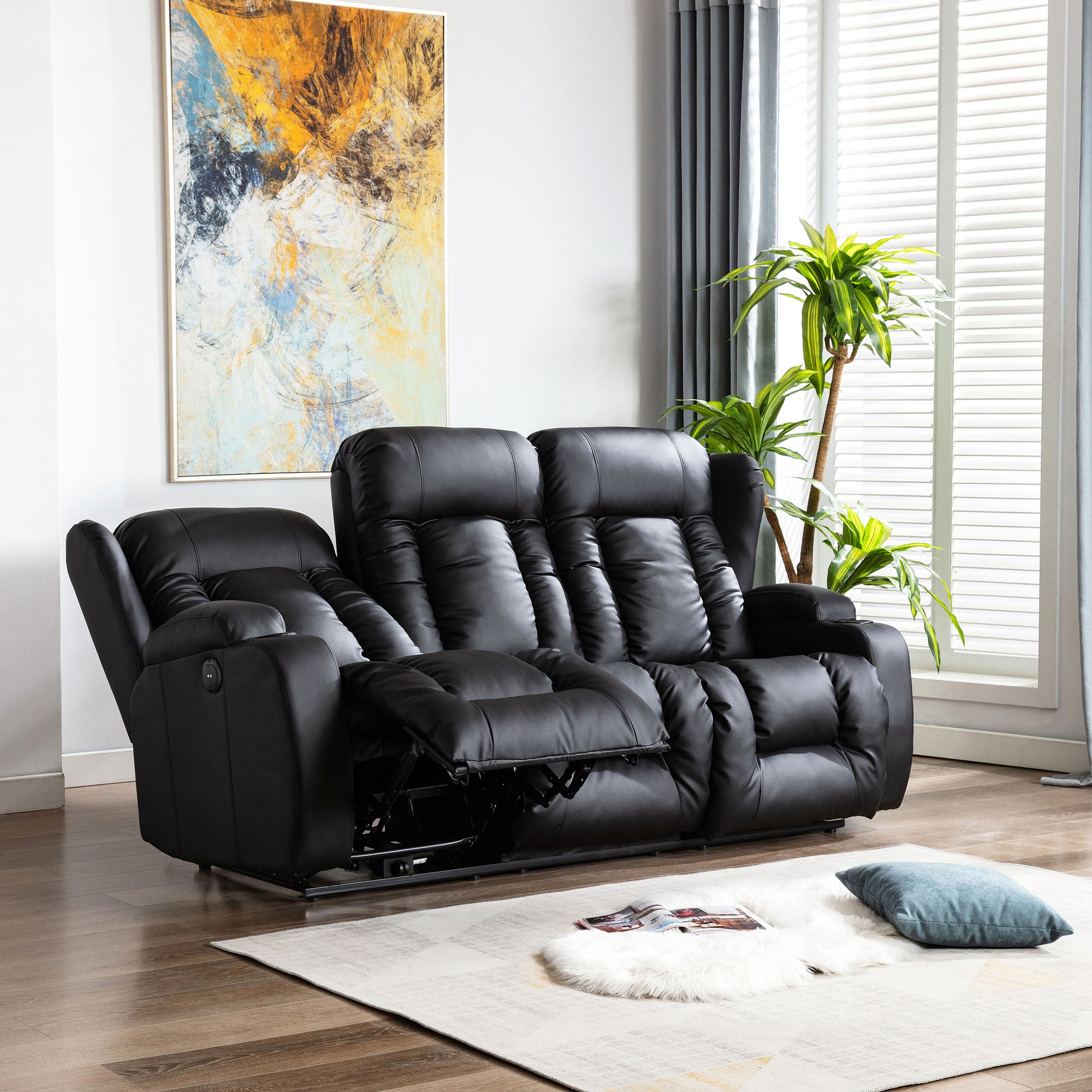 Black leather three-seater recliner sofa with one seat fully reclined, featuring cushioned backrests, cupholders, and vertical stitching, in a living room with wooden flooring and abstract wall art.