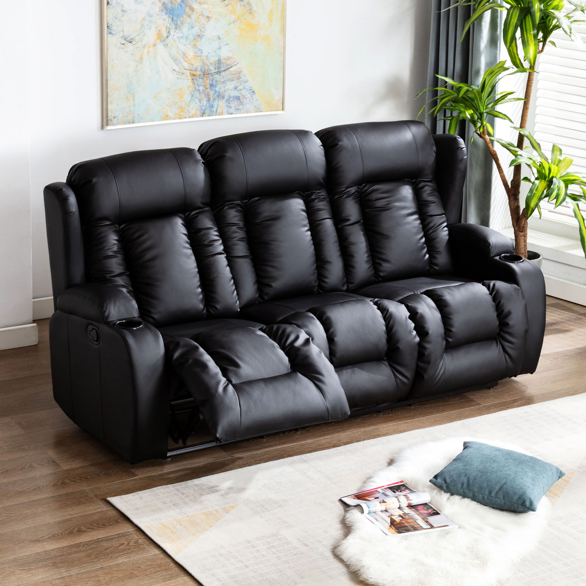 Black leather three-seater manual recliner sofa with one seat partially reclined, featuring cushioned backrests, cupholders, and vertical stitching, in a living room with wooden flooring and abstract wall art.