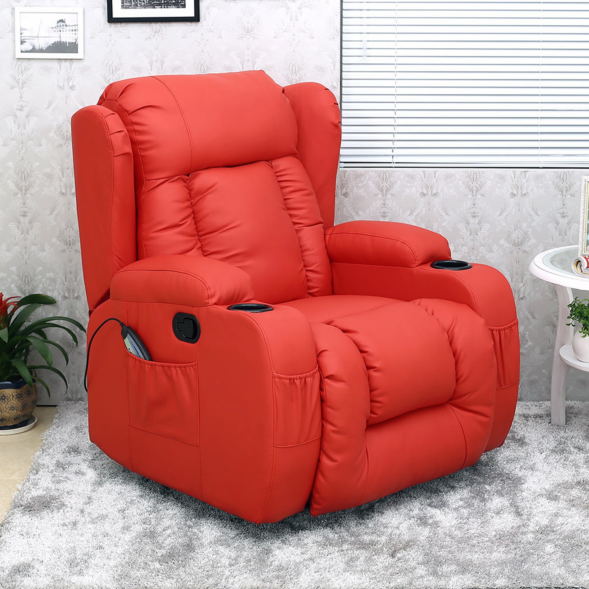 Red leather manual recliner with a cushioned backrest featuring vertical stitching, padded armrests, cup holders, and a single side pocket, set in a living room with a patterned wall and light grey rug.