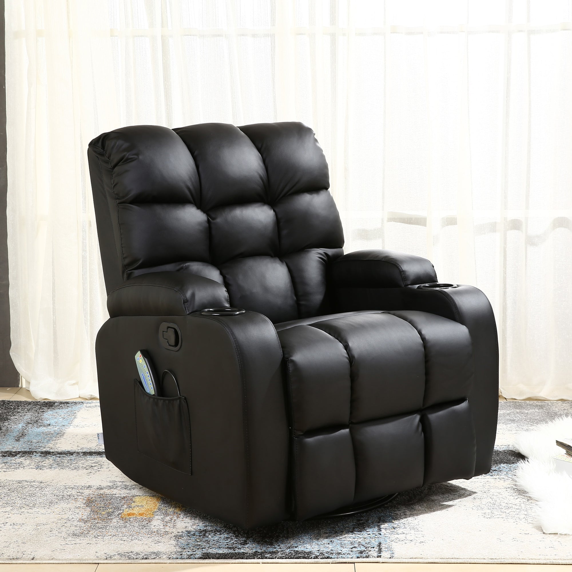 Black leather manual recliner with tufted backrest, cup holders, and a side pocket, set in a living room with light curtains and a patterned rug. A book and a magazine rest on the floor nearby.