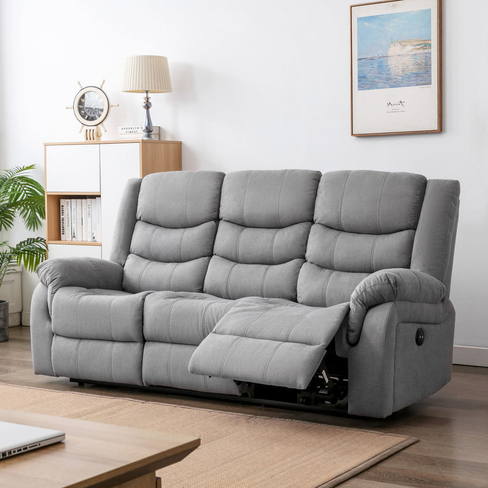 Grey fabric three-seater electric reclining sofa with one seat extended, placed in a cosy living room with light wooden furniture, a nautical clock, and framed artwork.