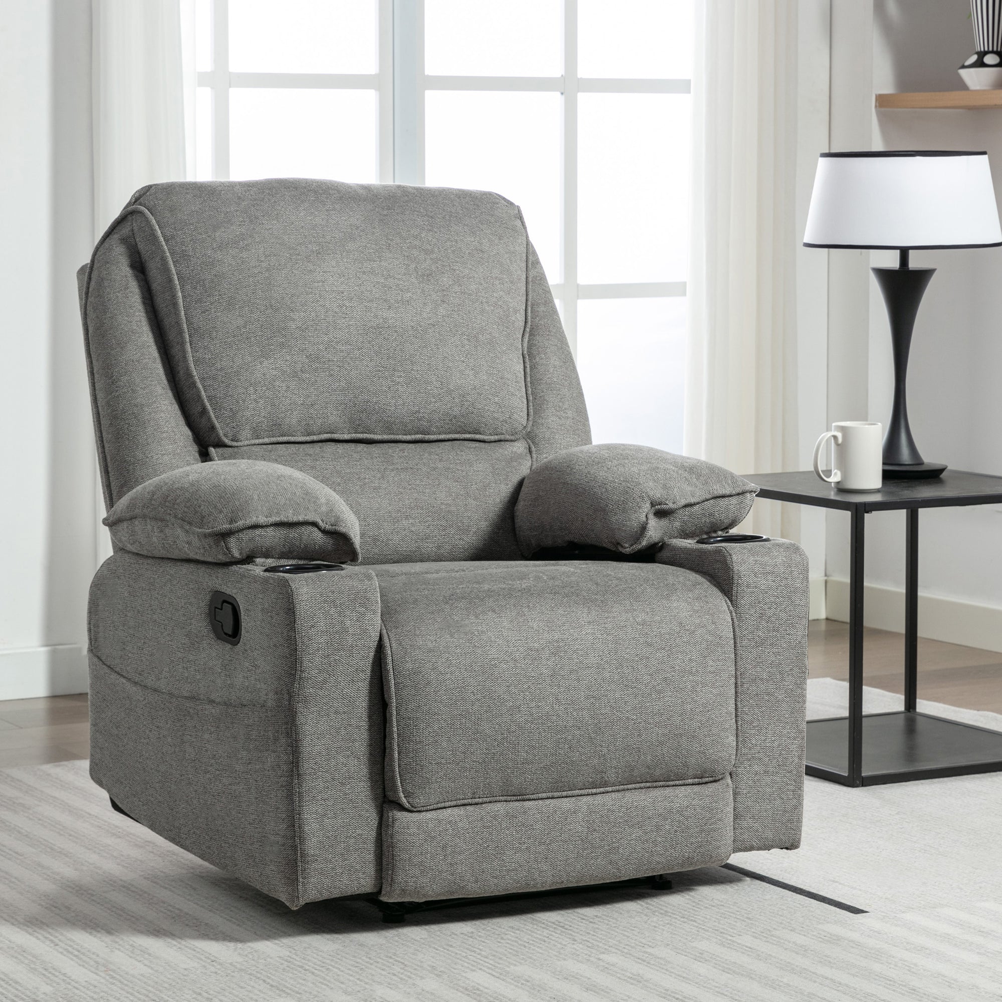 Grey fabric manual recliner chair with padded armrests, set on a light-coloured rug in a modern living room near a black side table.