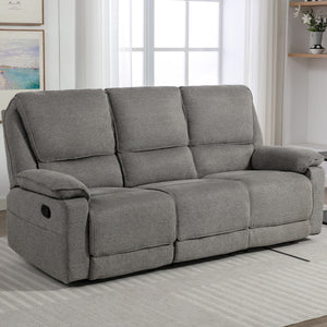 Grey fabric manual reclining three-seater sofa with padded armrests, positioned on a light-coloured rug in a living room near large windows.