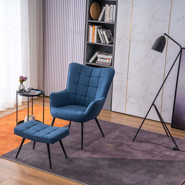 A blue linen accent chair with a matching footstool, both with black tapered legs, positioned in a room with a floor lamp, side table, and bookshelf.