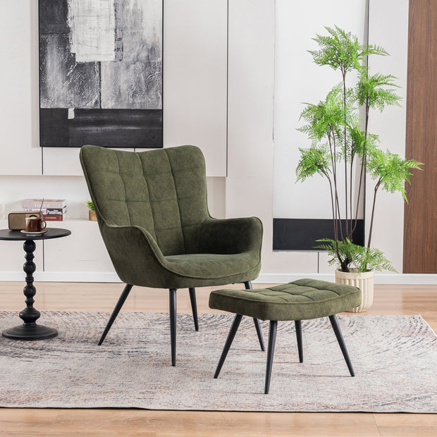 A green velvet accent chair with a matching footstool, both featuring black tapered legs, set in a modern room with a black-and-white abstract painting, potted plant, and side table.
