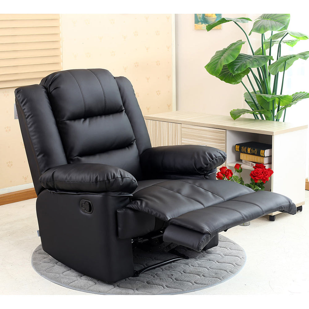A black manual recliner chair in a semi-reclined position, set on a grey circular rug next to a side table with books and plants, in a cosy room.