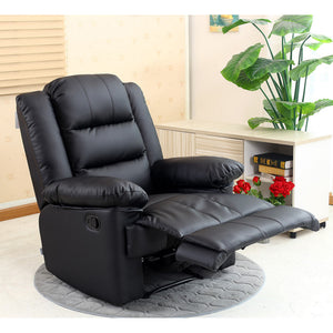 A black manual recliner chair in a semi-reclined position, set on a grey circular rug next to a side table with books and plants, in a cosy room.