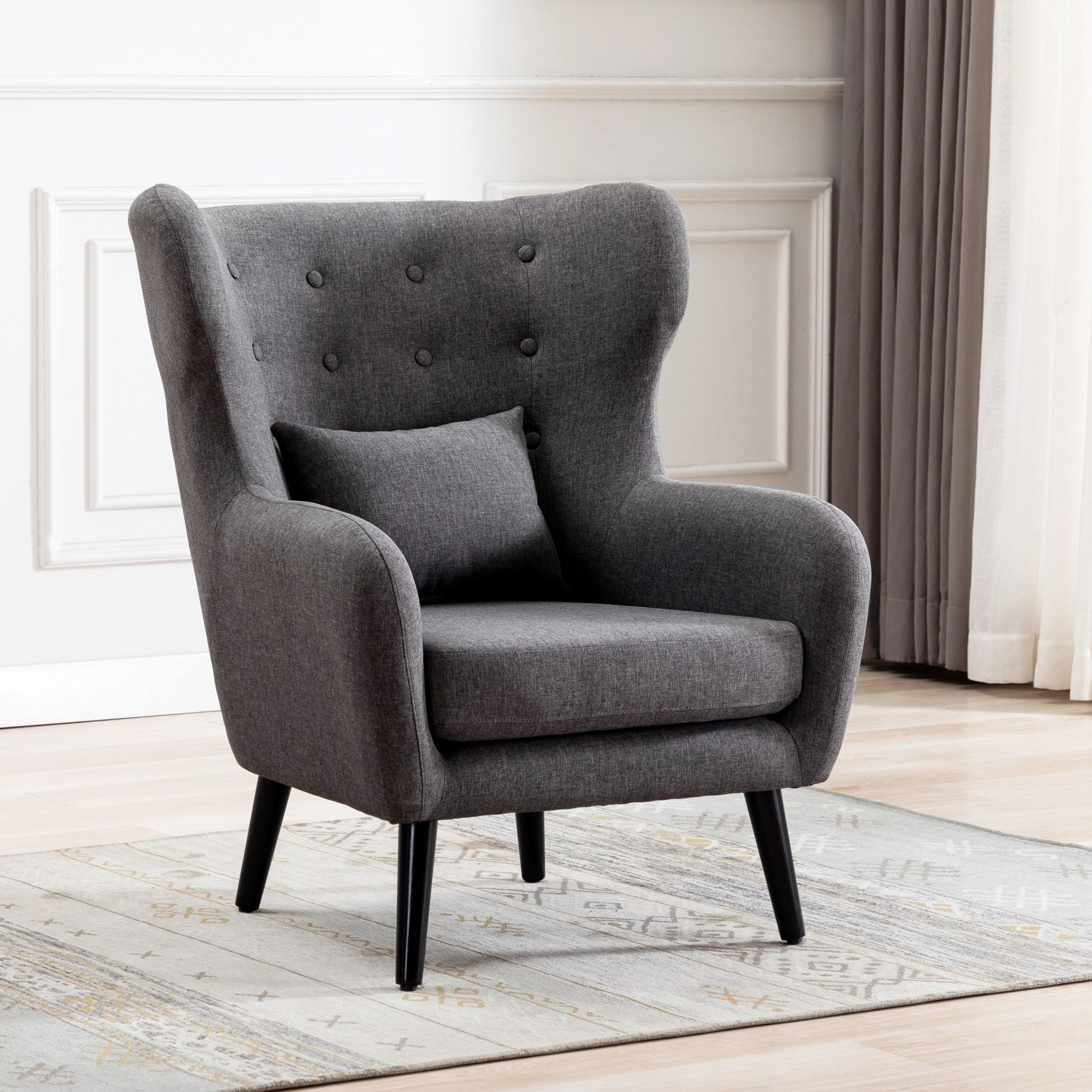Grey linen accent wingback chair with tufted buttons, set on a grey patterned rug against a white panelled wall.