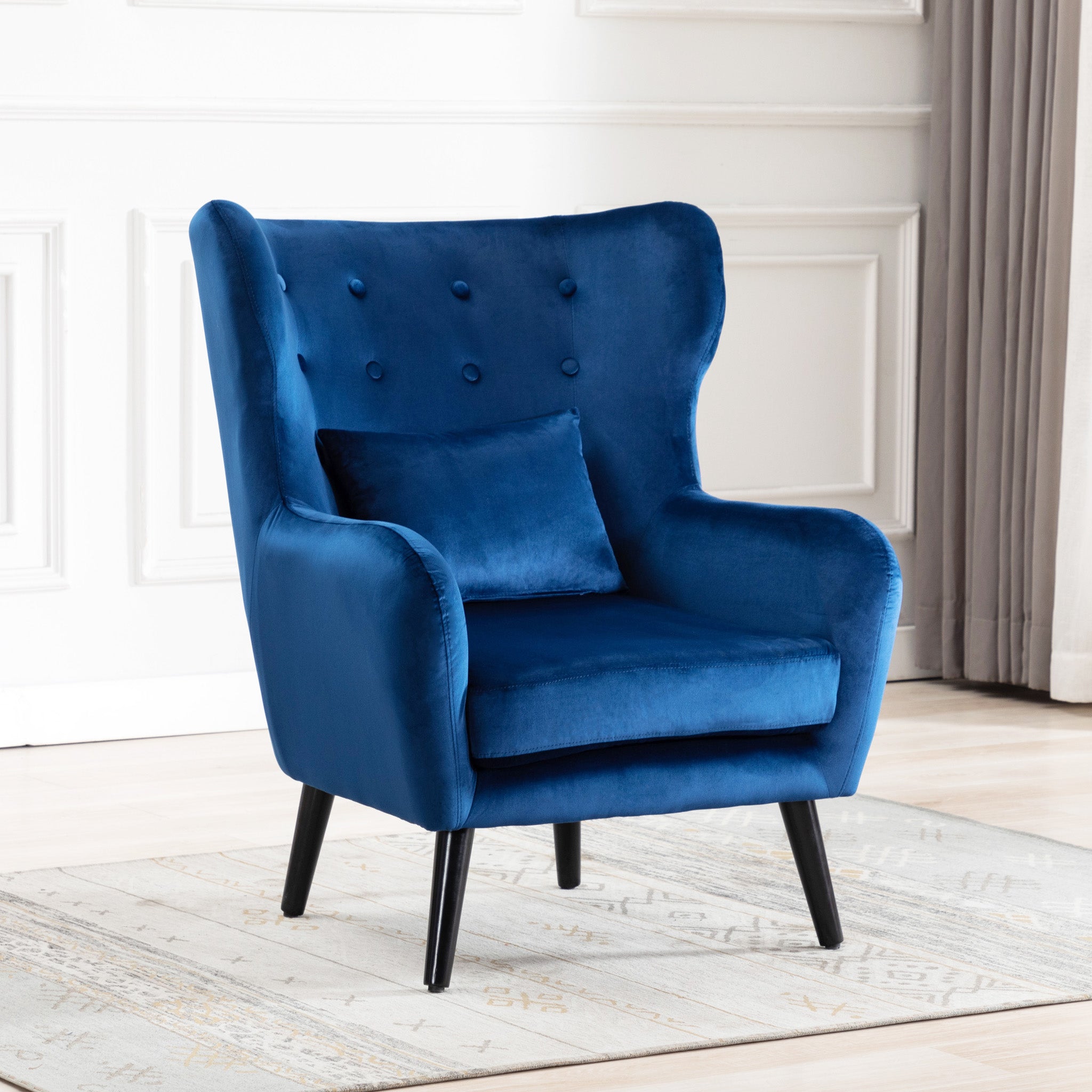 Blue velvet accent wingback chair with tufted buttons, set on a grey patterned rug against a white panelled wall.
