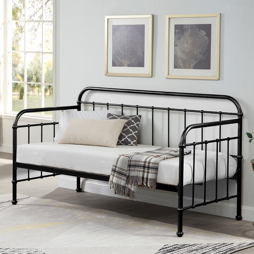 A black metal day bed is adorned with white bedding, decorative pillows, and a plaid throw blanket. Two paintings hang above the bed.