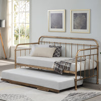 A white bedroom featuring a brass metal day bed with a trundle, white bedding, decorative pillows, and a plaid throw blanket. Two framed tree artworks hang above.