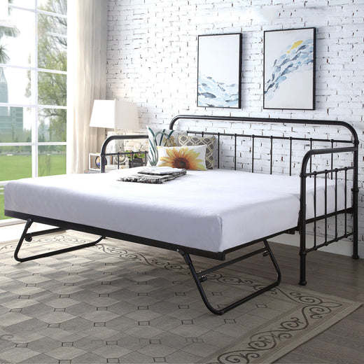 A foldable black metal bed with white linens and decorative cushions, with a modern brick wall background.