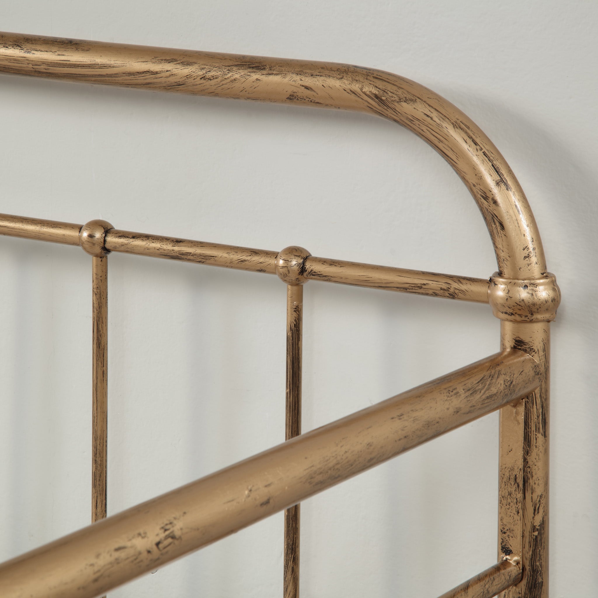 A close-up of the headboard of a brass-coloured metal bed, against a white wall.