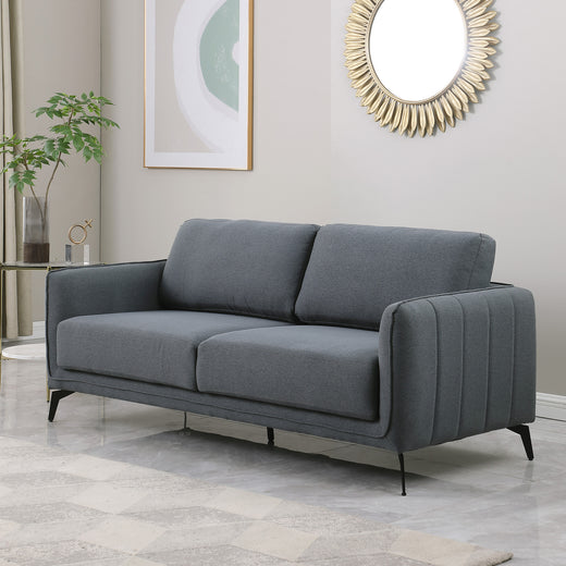 Dark grey fabric sofa with black metal legs in a grey living room, featuring a round sunburst mirror and a side table with flowers.