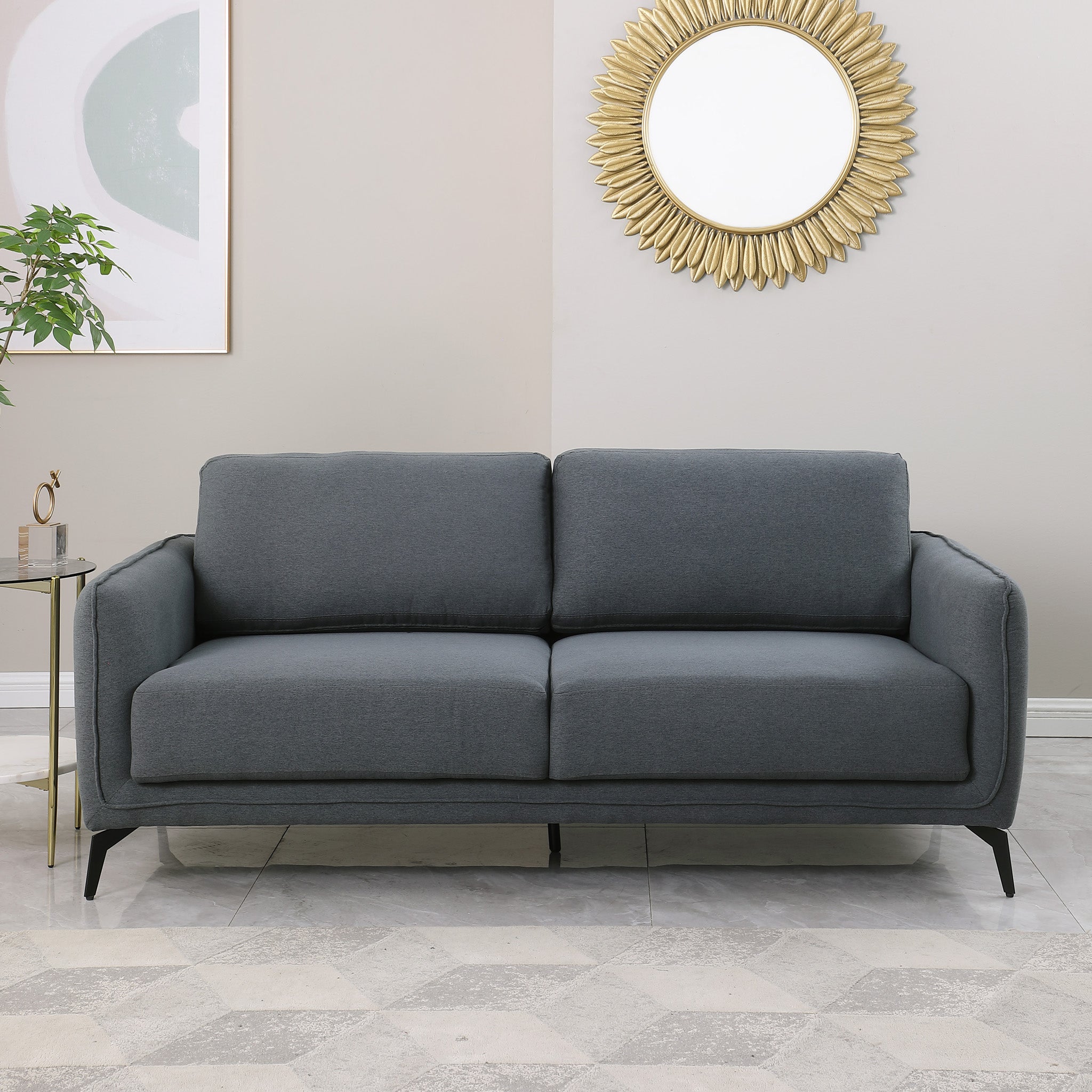 Dark grey upholstered sofa with black metal legs in a living room, featuring a round sunburst mirror and a side table with flowers.