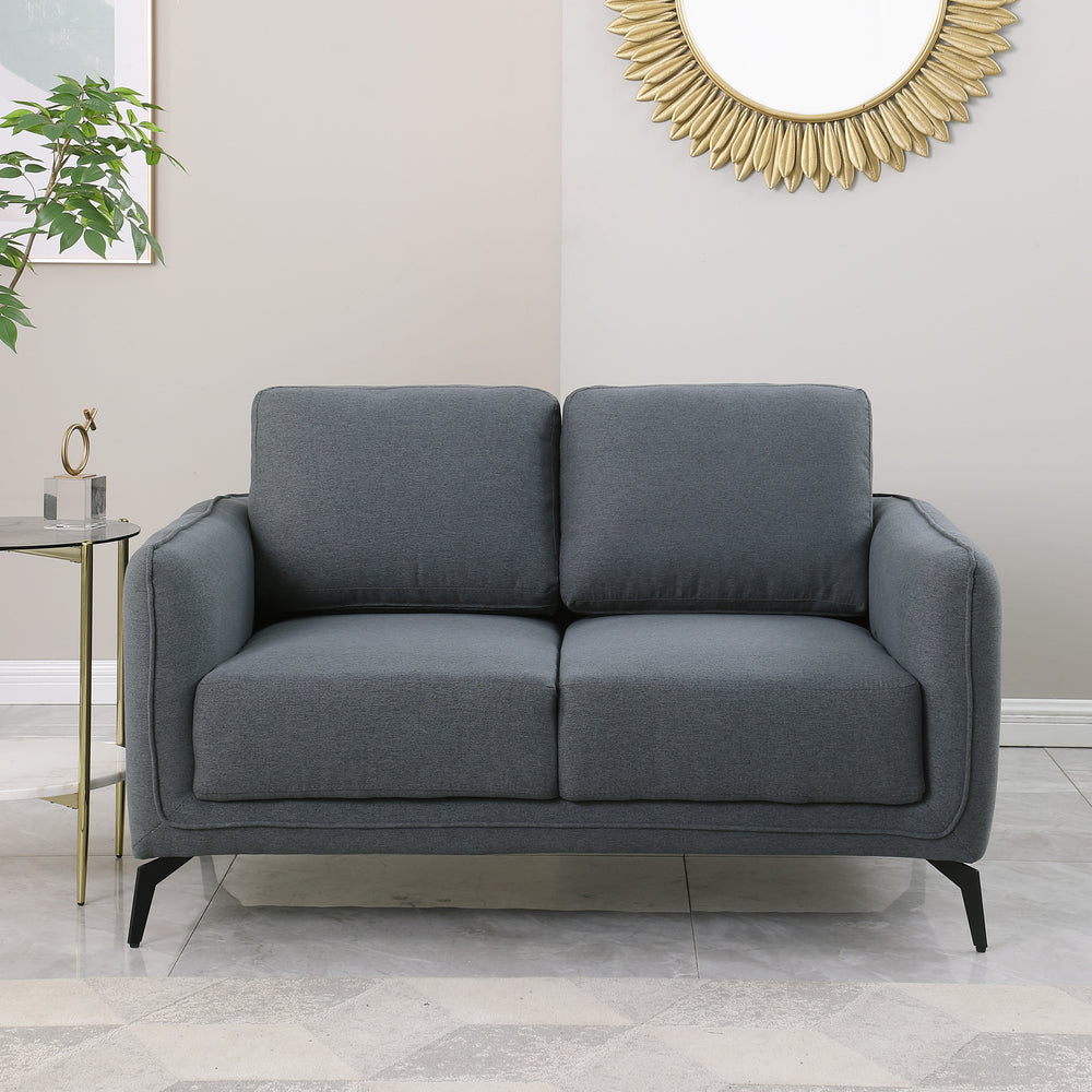 Dark grey upholstered sofa with black metal legs in a living room, featuring a round sunburst mirror and a side table with flowers.