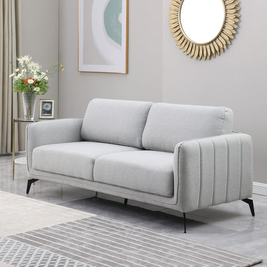 Light grey upholstered sofa with black metal legs in a grey living room, featuring a round sunburst mirror and a side table with flowers.