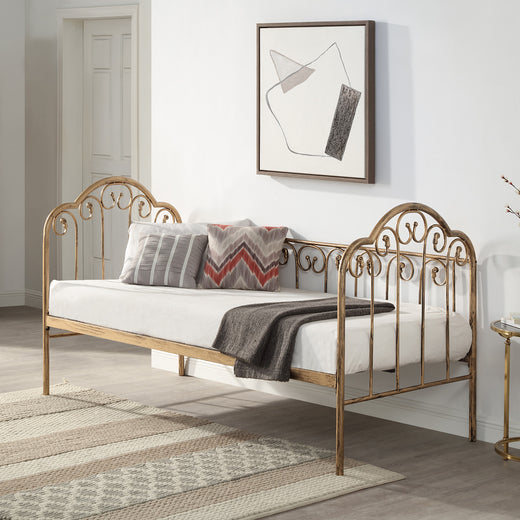 A brass-coloured metal day bed is adorned with white bedding, decorative pillows, and a grey throw blanket. A geometric painting hangs above the bed.