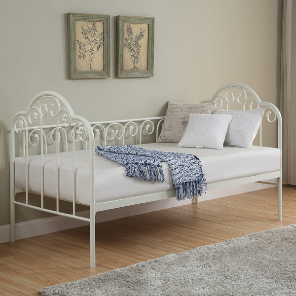 A white metal day bed is adorned with white bedding, decorative pillows, and a blue throw blanket. Two botanical paintings hang above the bed on a beige wall. 