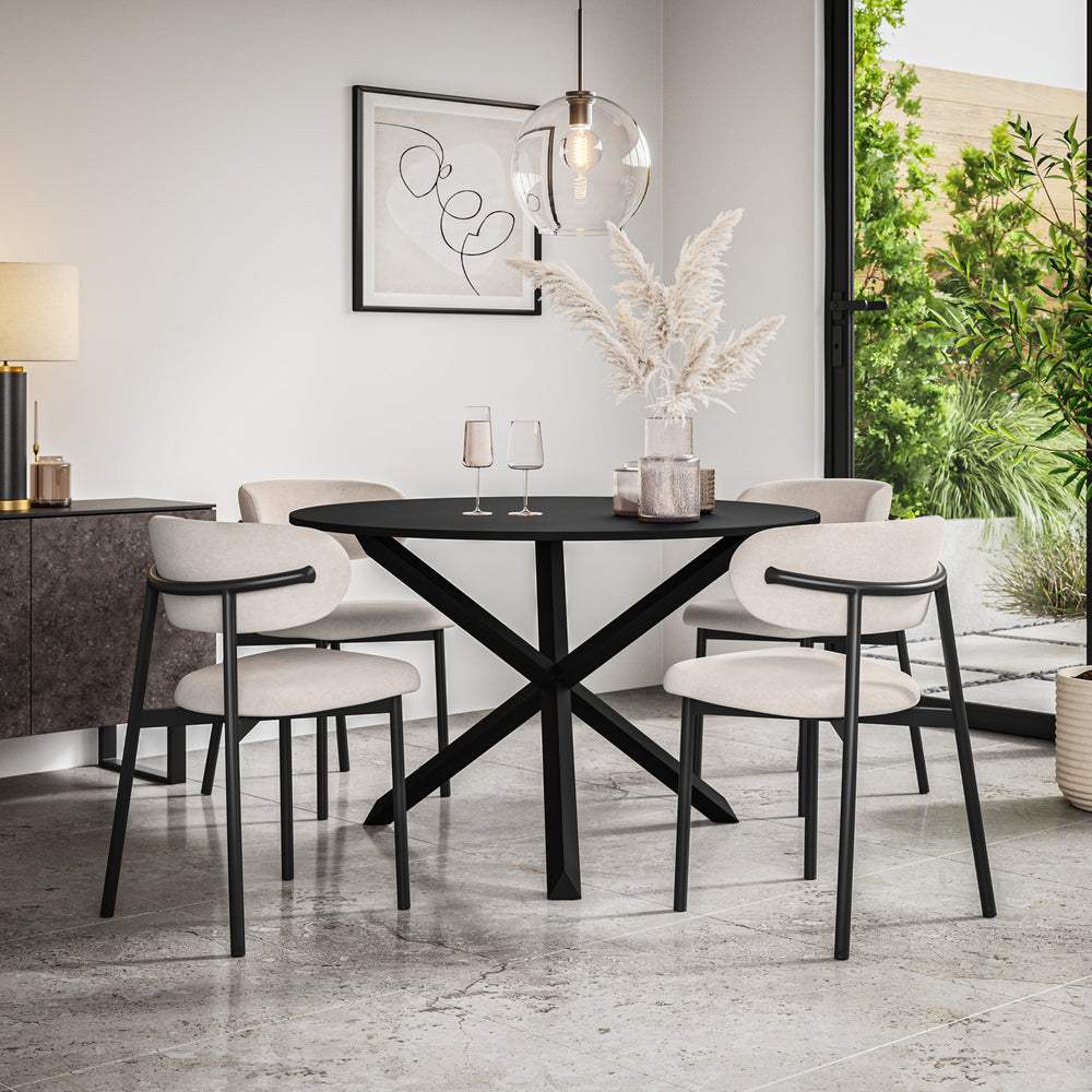 Black oval dining table with crossed base and four beige upholstered chairs in a dining room