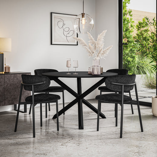 Black dining table with crossed pedestal base, surrounded by four dark upholstered chairs