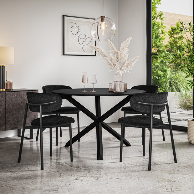 Black dining table with crossed pedestal base, surrounded by four dark upholstered chairs