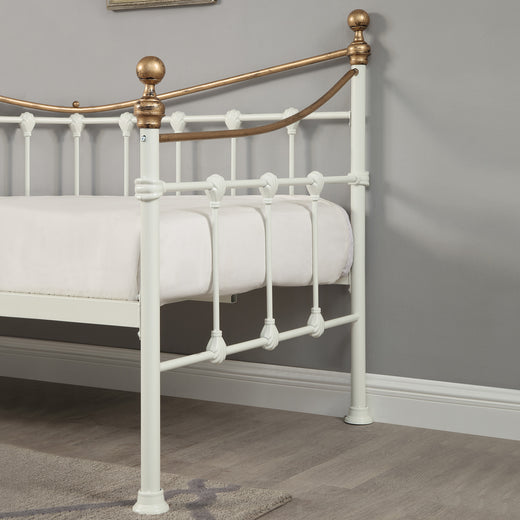 A close up view of the side of a white and brass metal day bed with a white mattress.