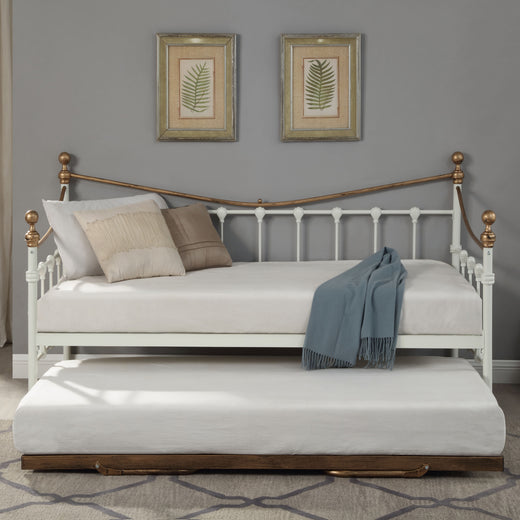  A brass and white metal day bed with an extended trundle is adorned with white bedding, decorative pillows, and a light grey throw blanket. Two botanical paintings hang above the bed. 