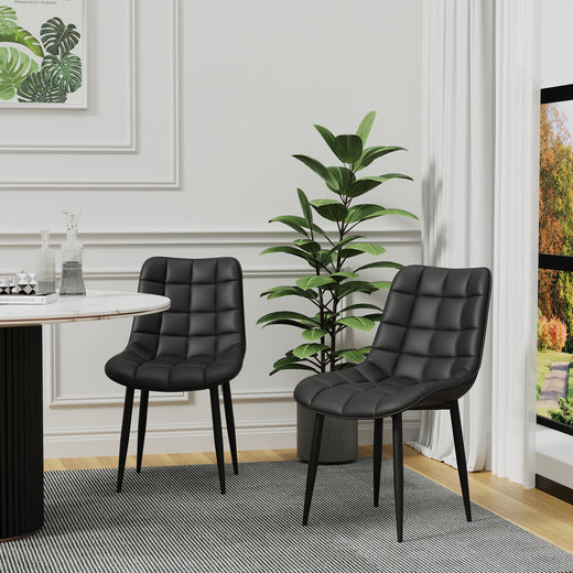 Two black tufted leather chairs with black legs on a gray patterned rug. A tall green plant and white walls with decorative molding are in the background.