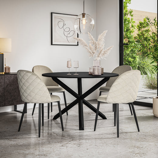 Black oval dining table with a crossed base and four beige quilted chairs in a dining room