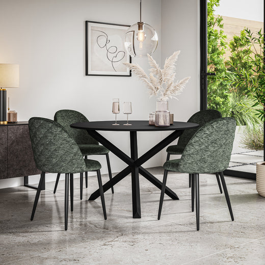 Black oval dining table with a crossed base and four green textured chairs in a dining room