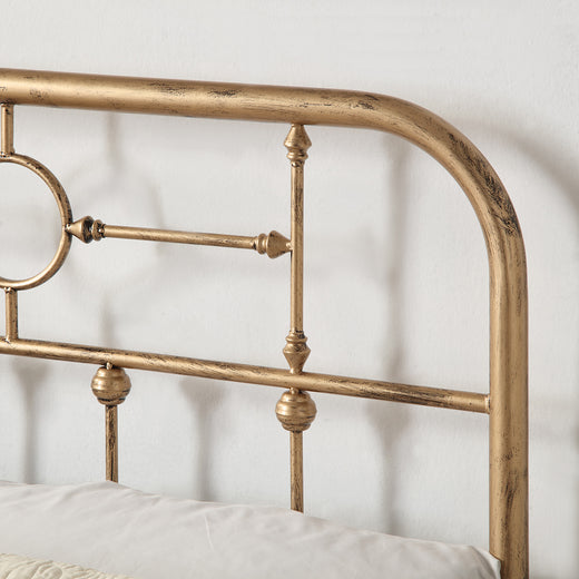 Close-up of a brass-coloured metal bed frame with circular designs and vertical bars, shown with part of a white pillow