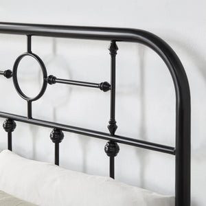 Close-up of a black metal headboard with circular designs and vertical bars. The headboard is shown with white pillows against it and a white background.